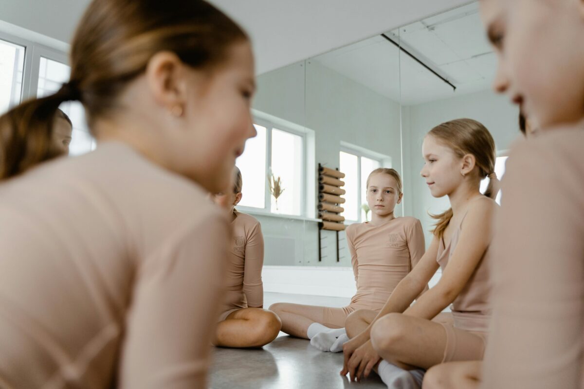 Merginų grupė meninės gimnastikos studijoje ilsisi ant grindų po treniruotės